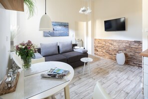 Ein modernes Wohnzimmer mit einem grauen Sofa, einem runden Esstisch mit Blumenvase, einem flachbildfernseher an der Wand und einer Holz-Akzentwand.
