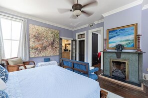A bedroom with a large bed, a chair, a fireplace, and a painting on the wall. - The General - Historic Pensacola Apt with Pool & Spa (Pensacola)