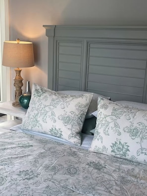 Ein Bett mit blumigem Bettzeug, ein Nachttisch mit Lampe und eine dekorative Vase.
