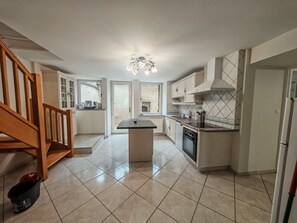 A modern kitchen with a central island, wooden staircase, and a view to the outside.