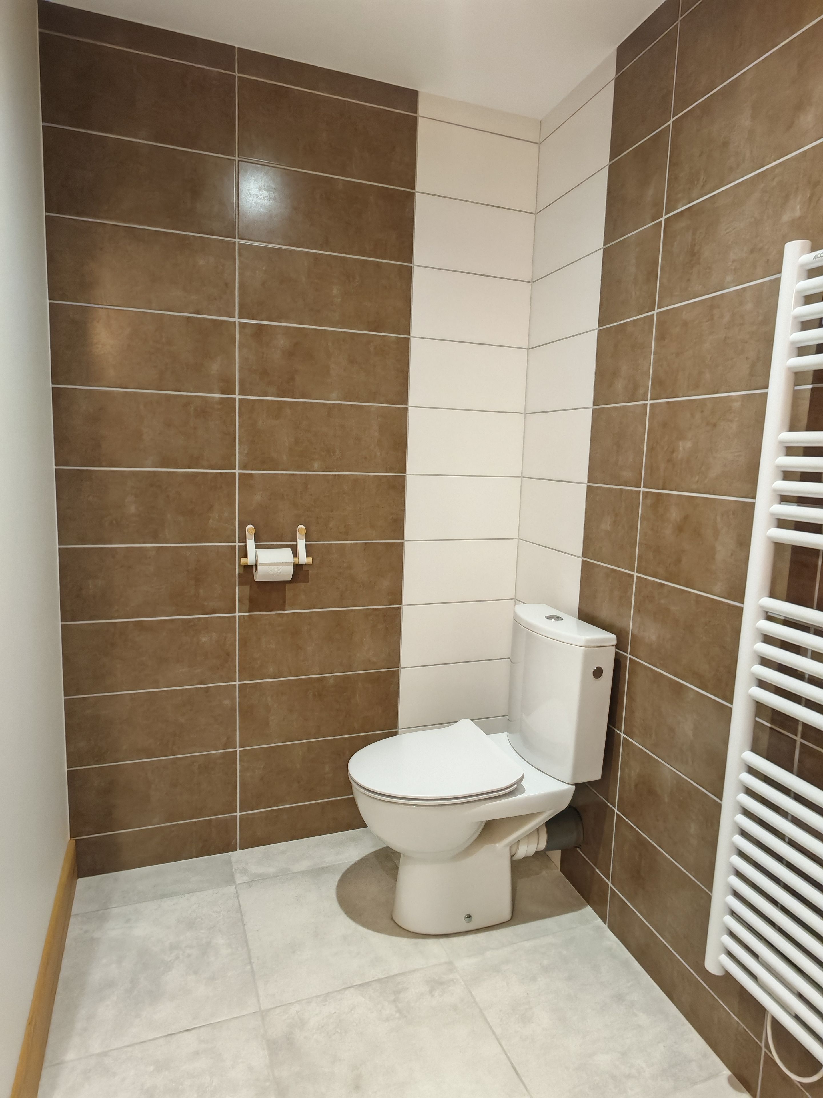 Une salle de bain avec des toilettes, un radiateur blanc et des carreaux marron et blancs.