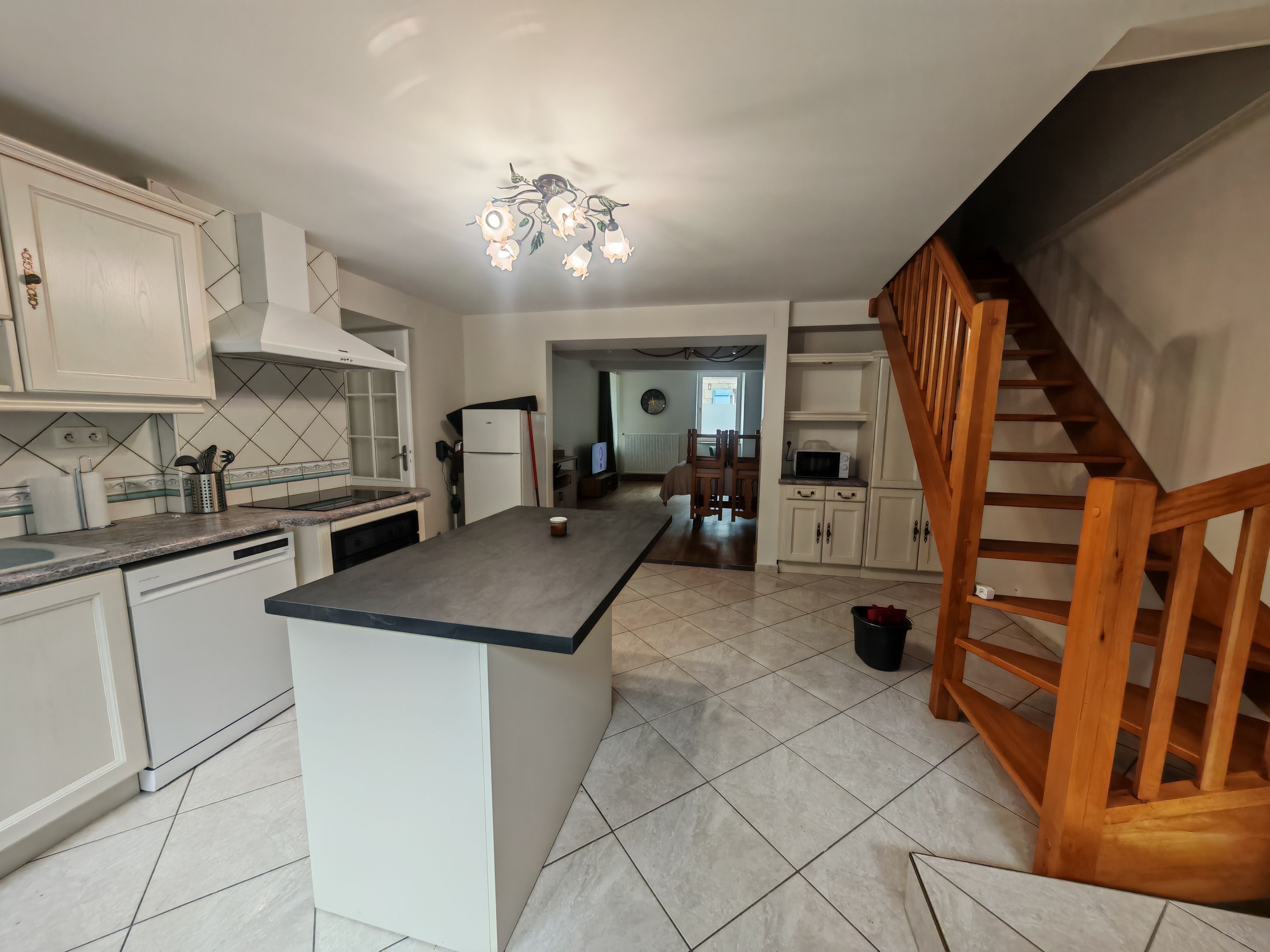A modern kitchen with a central island, white cabinetry, and a wooden staircase.