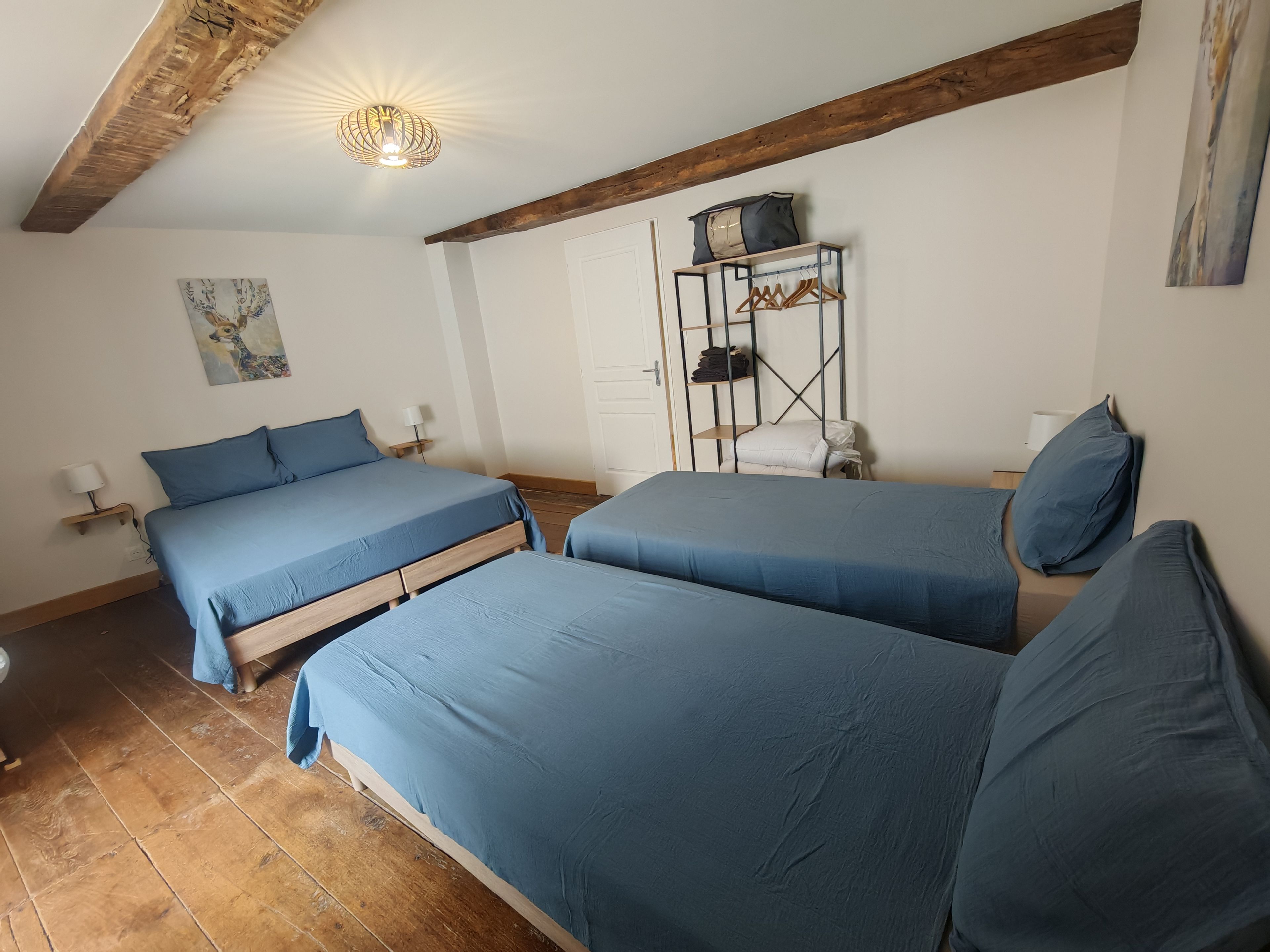 A room with two beds, a wooden ceiling, a wall-mounted shelf with clothes, and a painting.