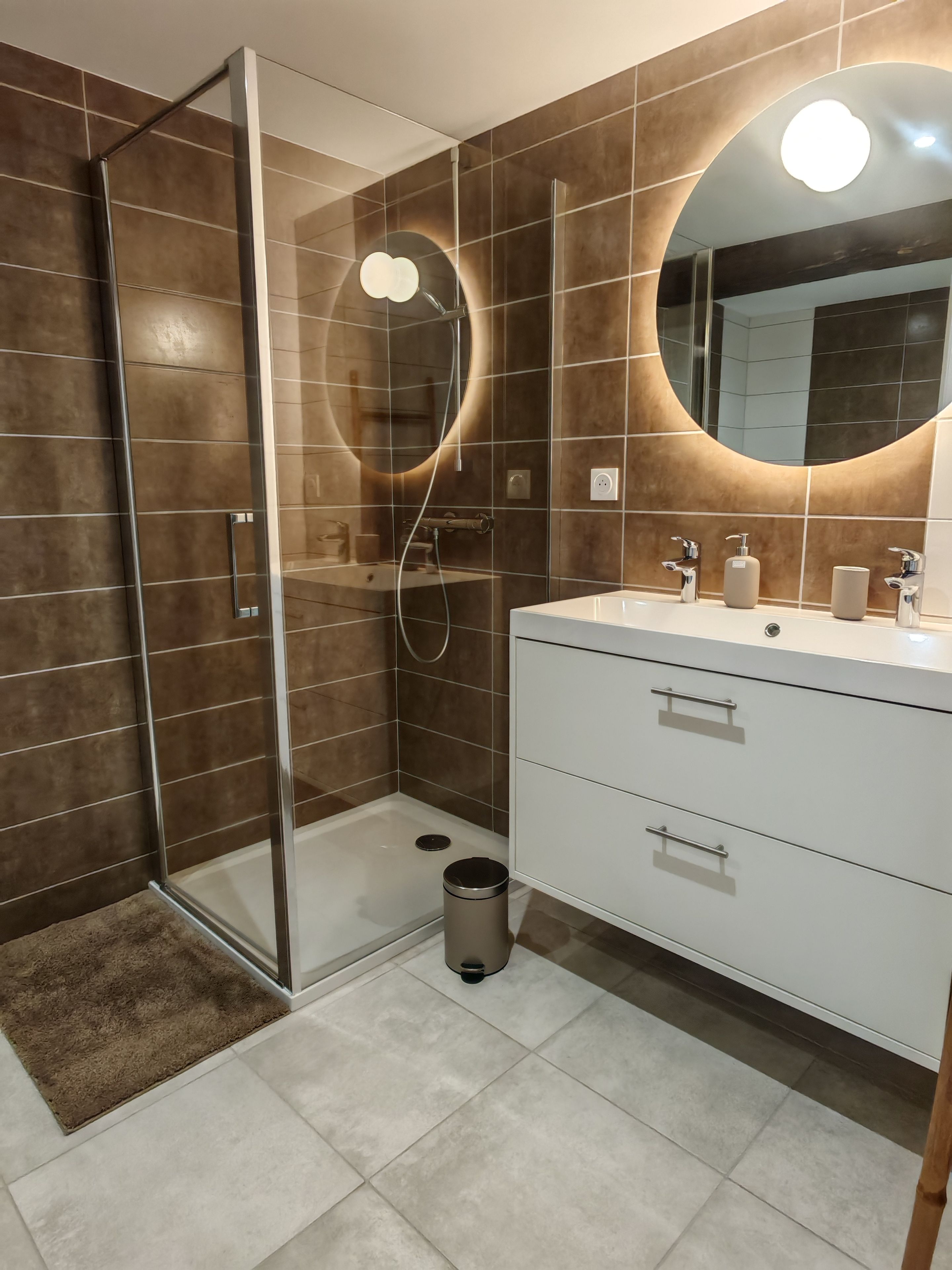 Een moderne badkamer met een douchecabine van glas, een wit wastafelmeubel met spiegel en een prullenbak.