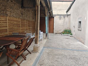 An outdoor patio with a wooden table and chairs, a hanging chair, and a small garden with flowers. - Vrbo Property (Châteauvillain)