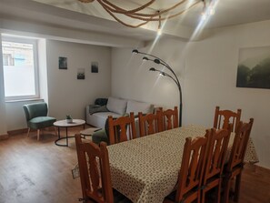 A room with a dining table, chairs, a sofa, a lamp, and a window.