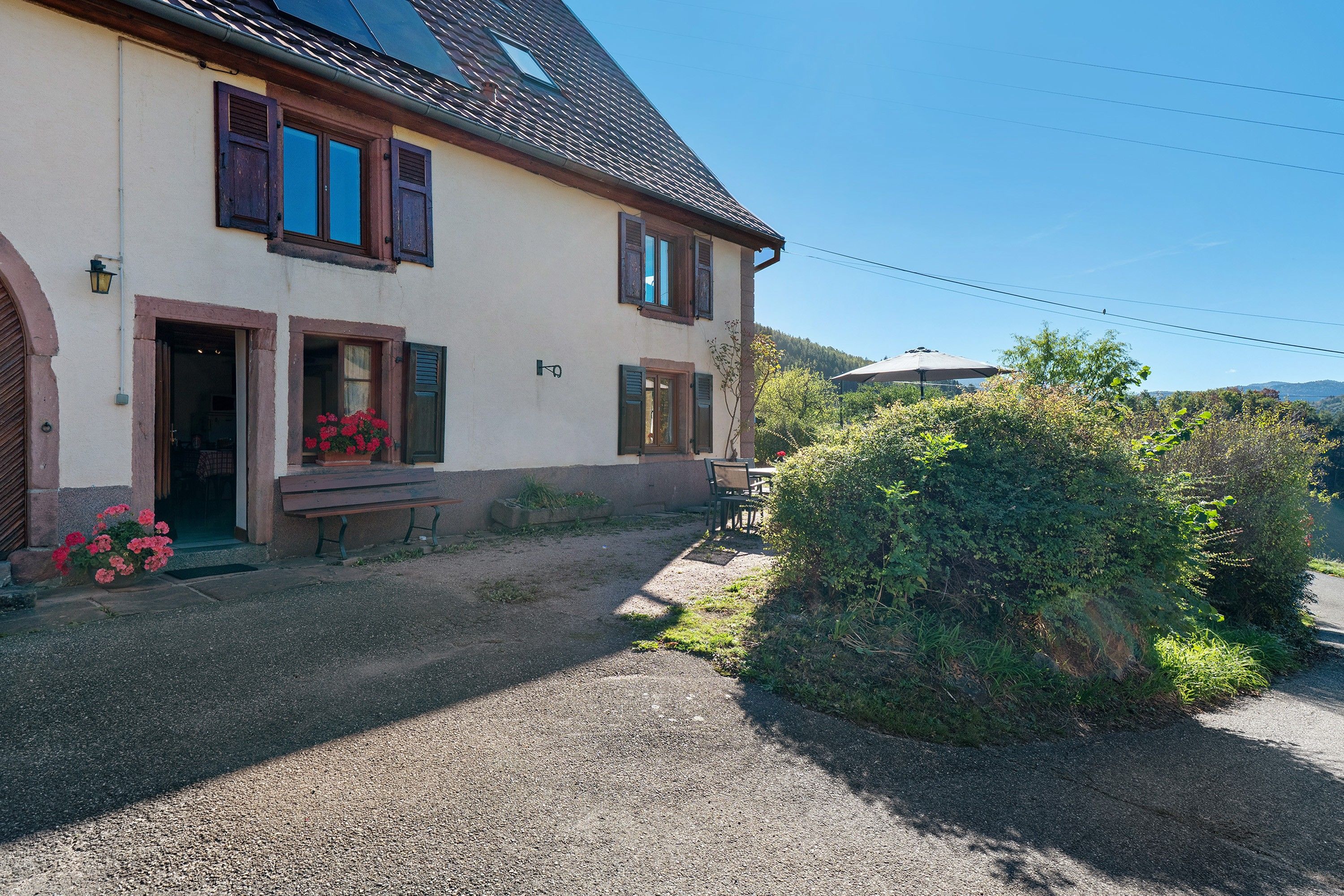 A two-story house with a gravel driveway and a bench outside.