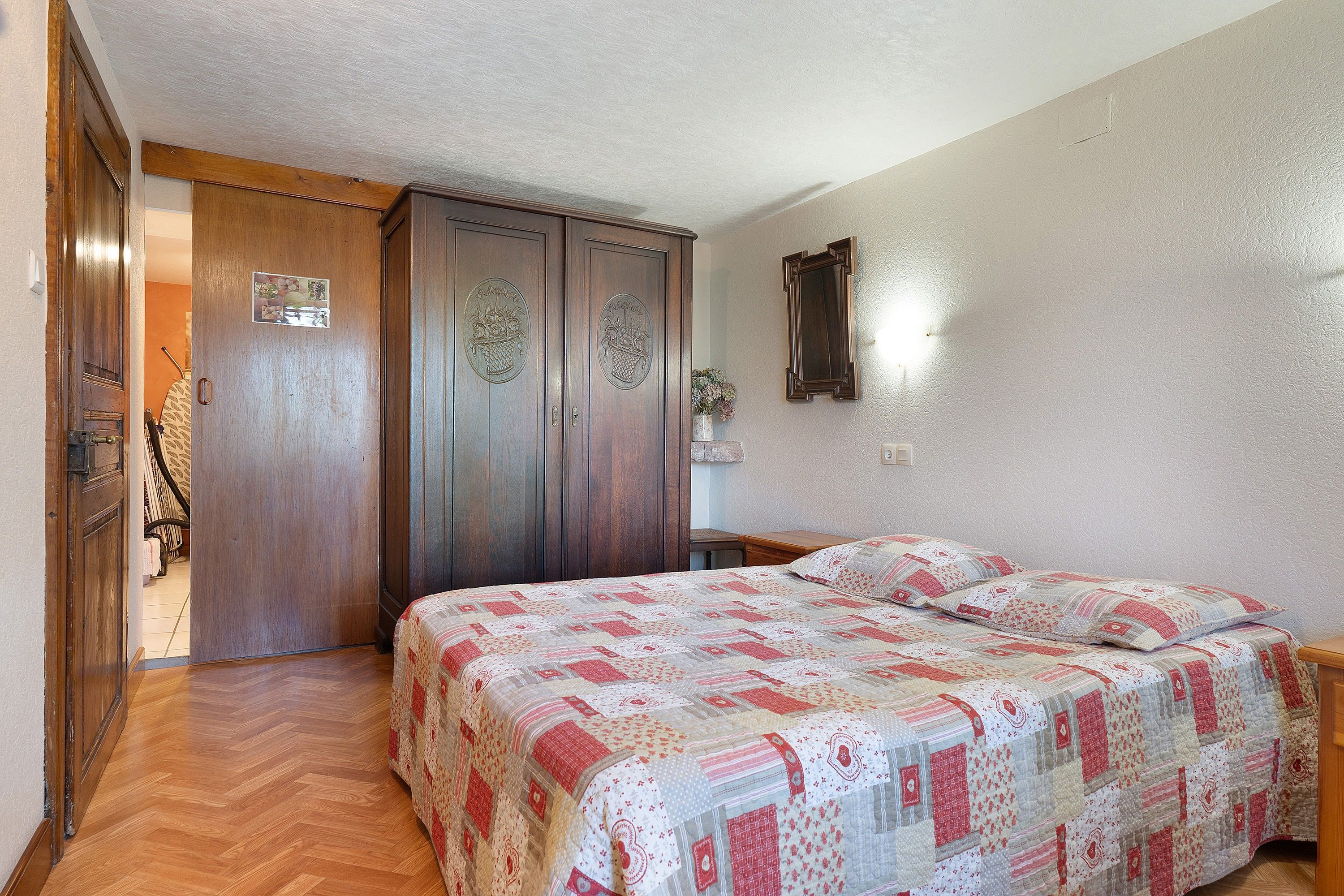 Un dormitorio con un armario de madera, una cama con colcha estampada y un espejo en la pared.