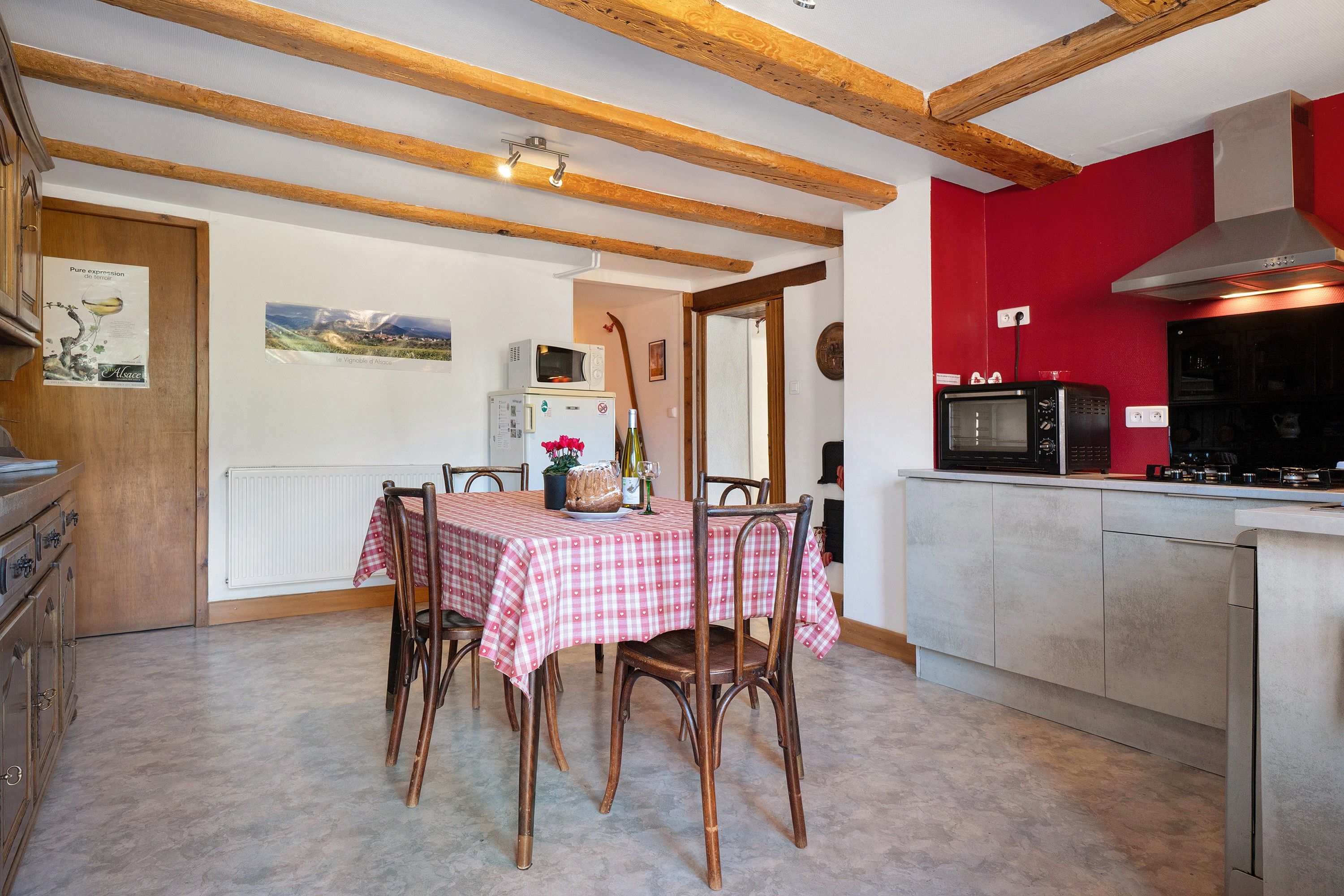 Une cuisine avec des poutres en bois, une table à manger avec des chaises, un mur rouge et un four à micro-ondes.