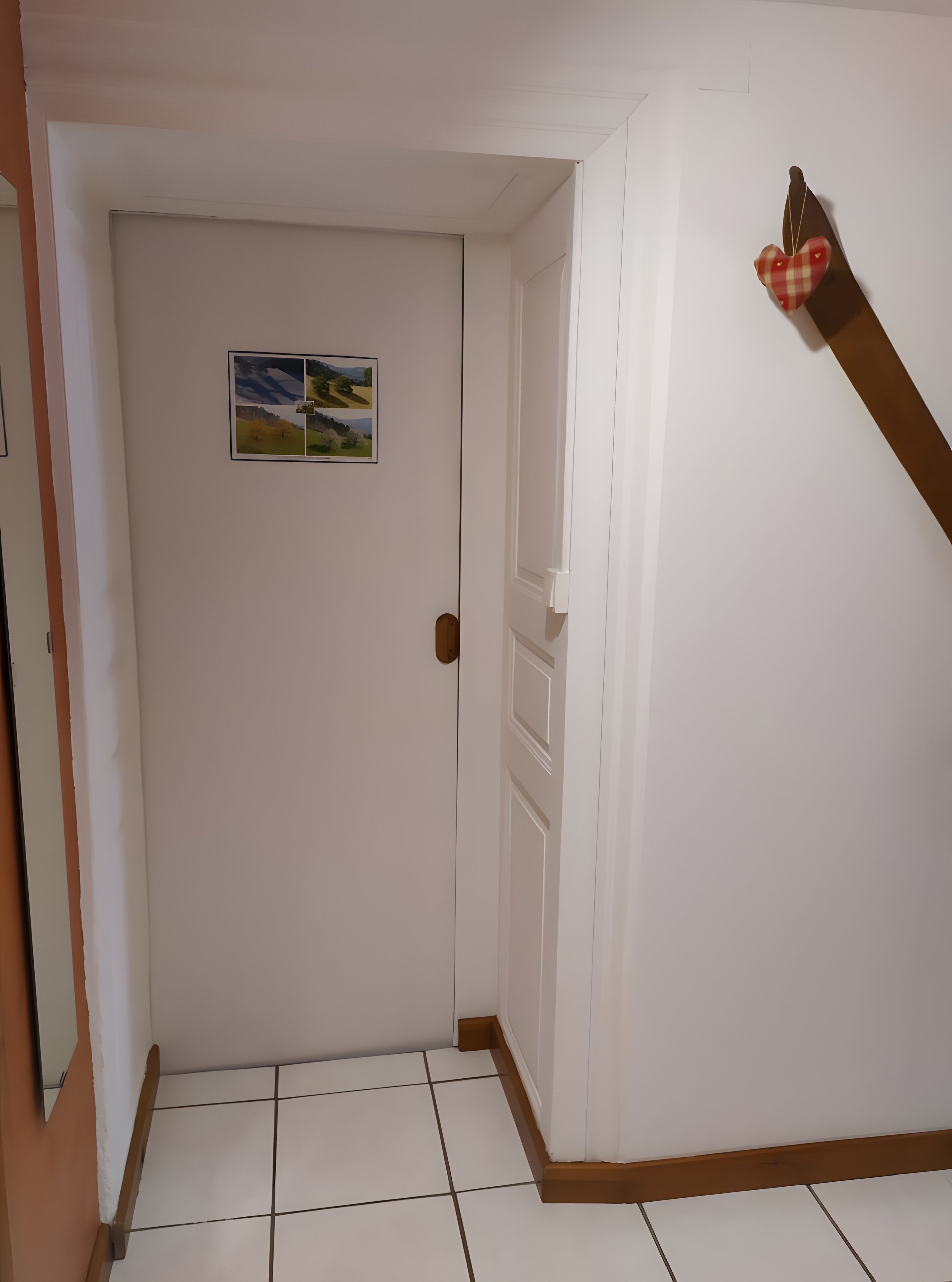 A hallway with a white door, a small landscape painting, and a wooden handrail.