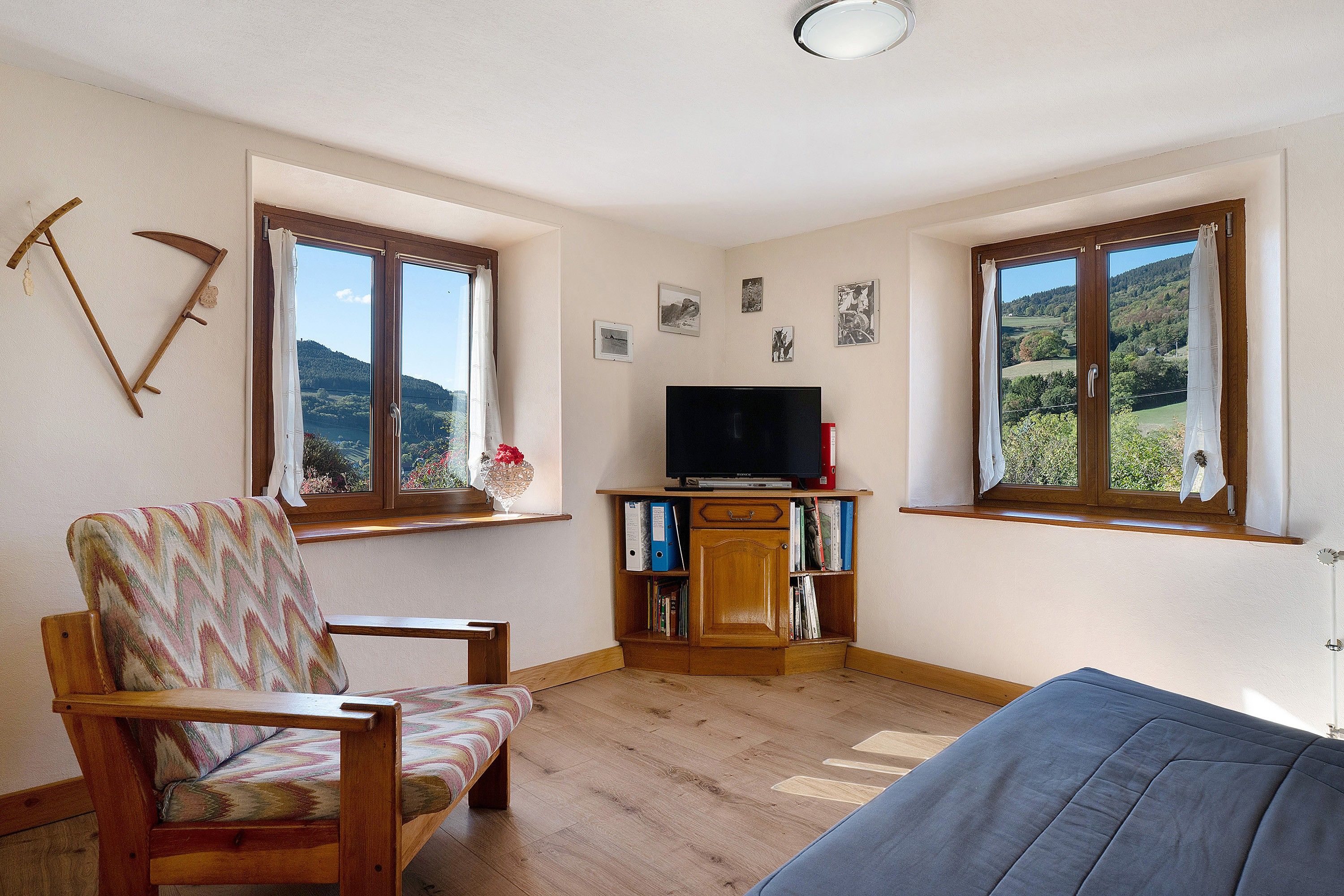 A room with a wooden chair, a sofa, a television on a wooden stand, and a bookshelf with books and binders.