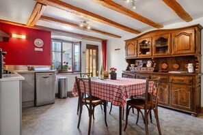 A kitchen with a dining table, wooden cabinets, and a red wall clock.