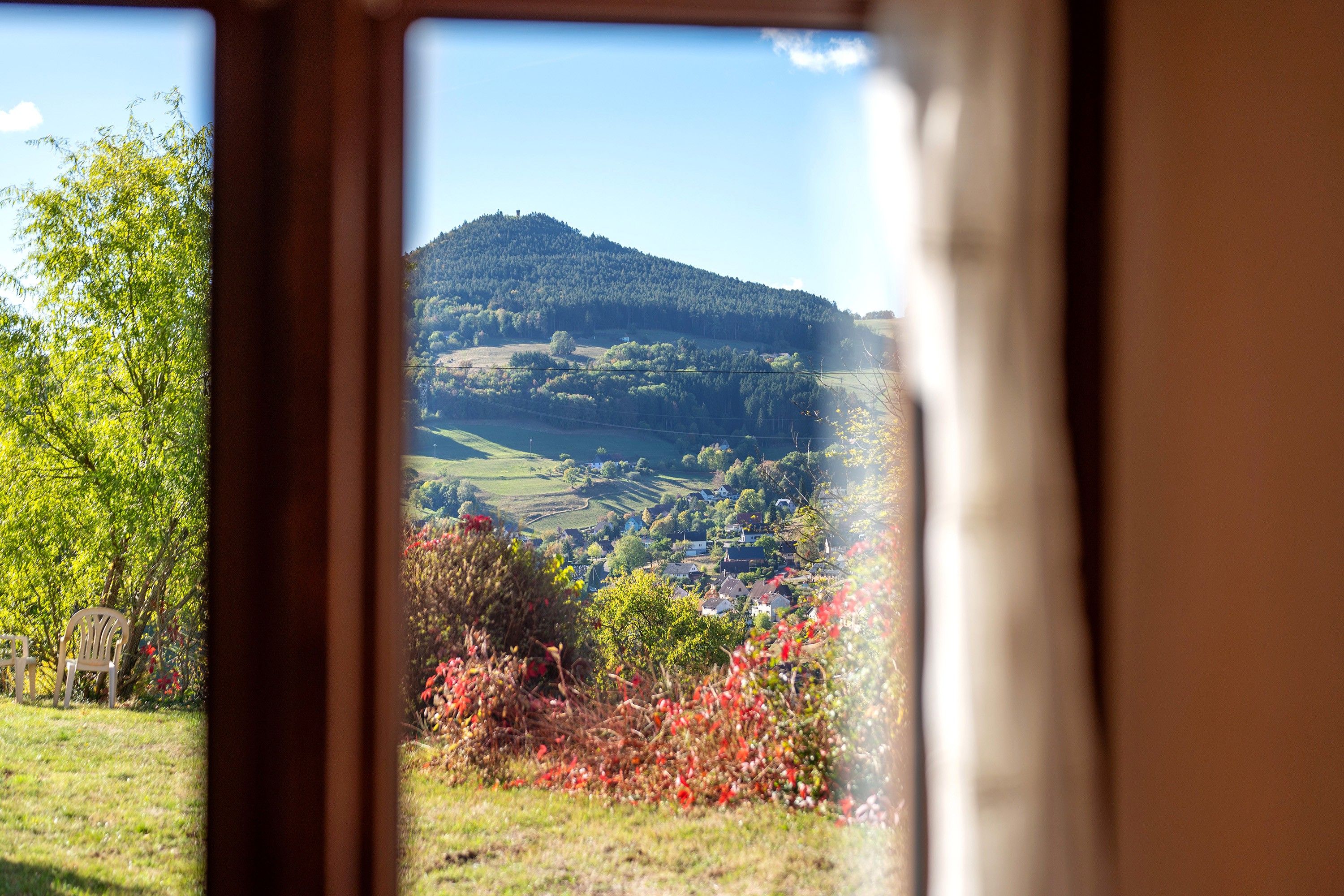 A view through a window of a rural landscape with a hill, fields, and a small village.