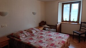 Une chambre à coucher comprenant un lit, une table de chevet, une chaise en bois, une fenêtre avec des rideaux et un luminaire fixé au mur.
