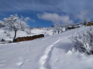 A snow-covered landscape with a clear sky, a stone wall, and a few buildings in the background.