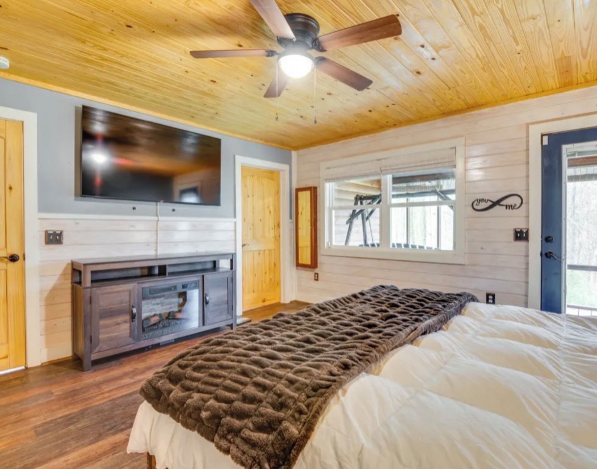 A bedroom with a bed, a television, a ceiling fan, and a window.