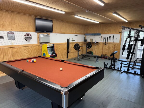 A pool table with balls, a television mounted on the wall, and a weightlifting area with equipment.