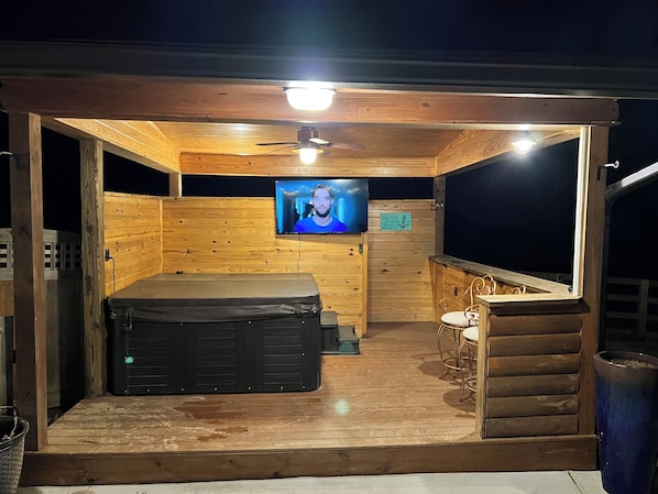 A wooden cabin with a hot tub, a television, and a bar area.