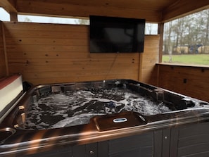 A hot tub with a control panel, a television mounted on the wall, and a window with a view of the outdoors.
