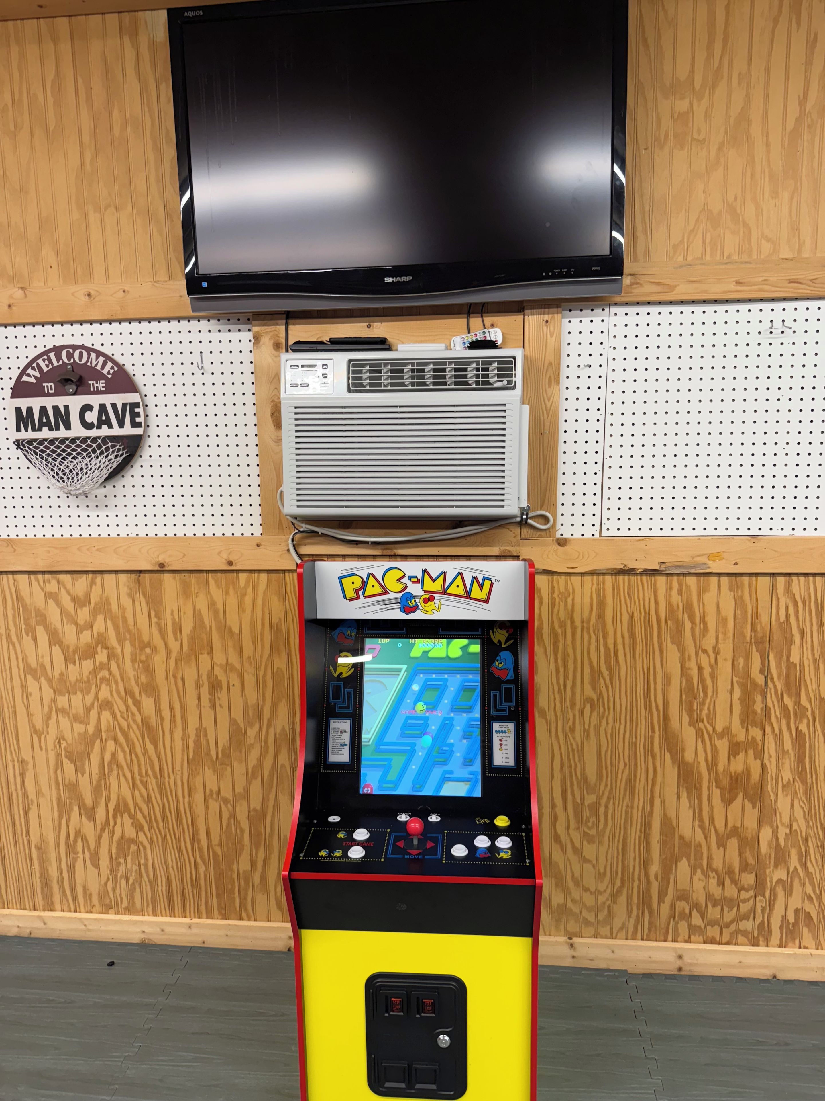 Una màquina recreativa de Pac-Man, un televisor i un cartell penjat a la paret.