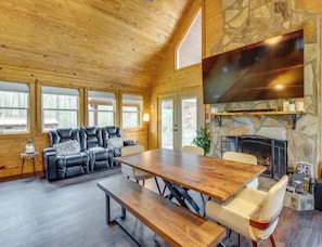 A spacious room with a large wooden table, a stone fireplace, and a leather sofa.