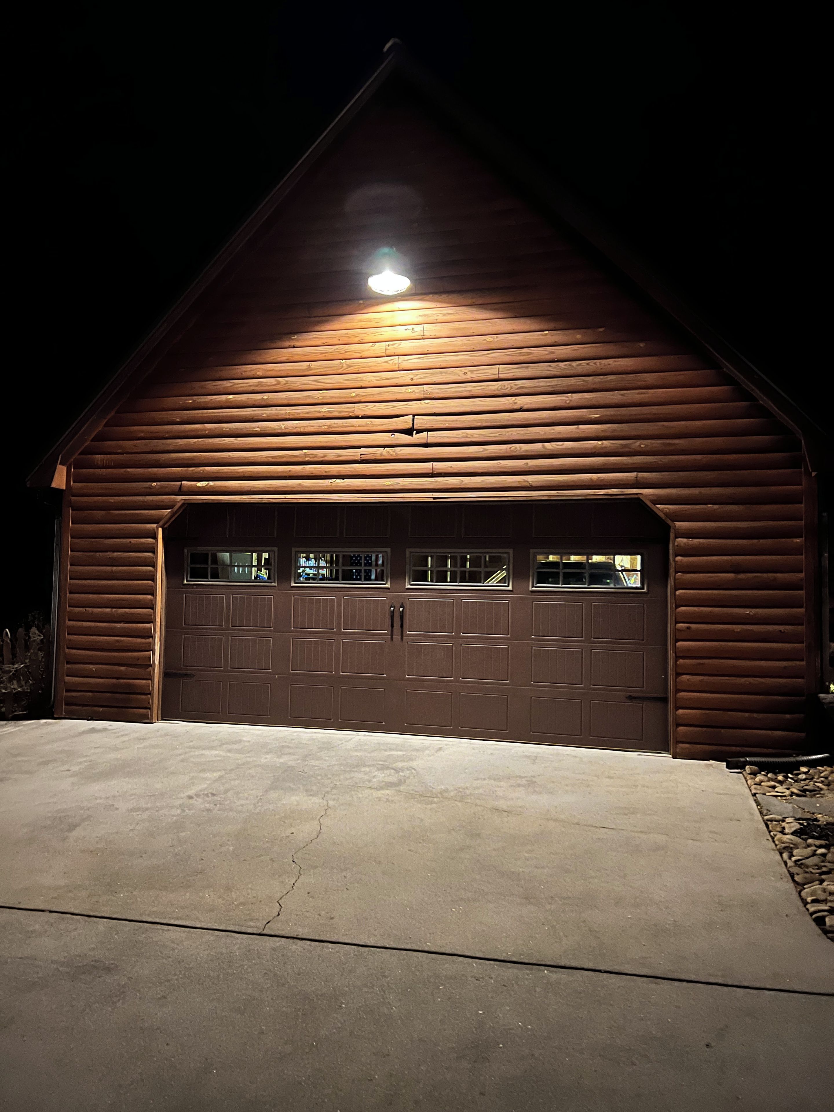 Um edifício de madeira com uma porta de garagem, entrada para carros e uma única luminária sobre a porta.