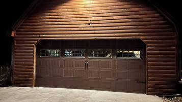 Um edifício de madeira com uma porta de garagem, entrada para carros e uma única luminária sobre a porta.