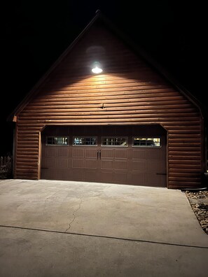 Um edifício de madeira com uma porta de garagem, entrada para carros e uma única luminária sobre a porta.