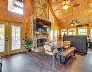 A spacious room with a stone fireplace, wooden ceiling, and large windows.