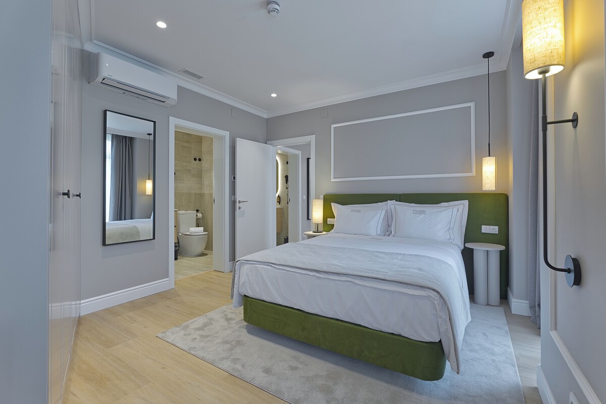 Un dormitorio moderno con cabecera verde, cama grande, mesita de noche y espejo.