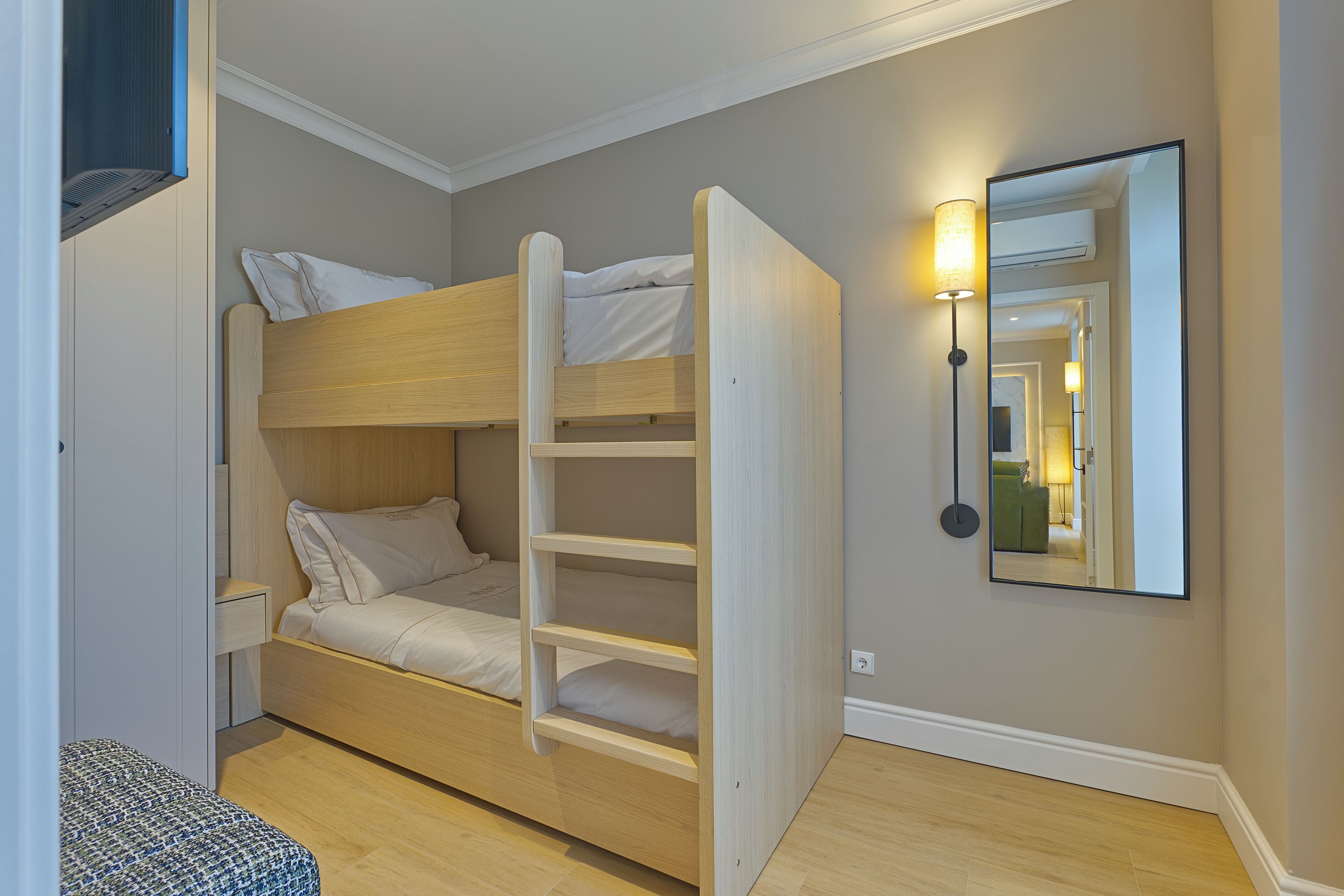 A bunk bed with a ladder, a bedside table, and a wall-mounted lamp.