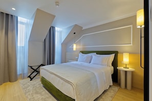 Una habitación de hotel moderna con una cama bien hecha, una mesita de noche con lámpara y un gran ventanal con cortinas.