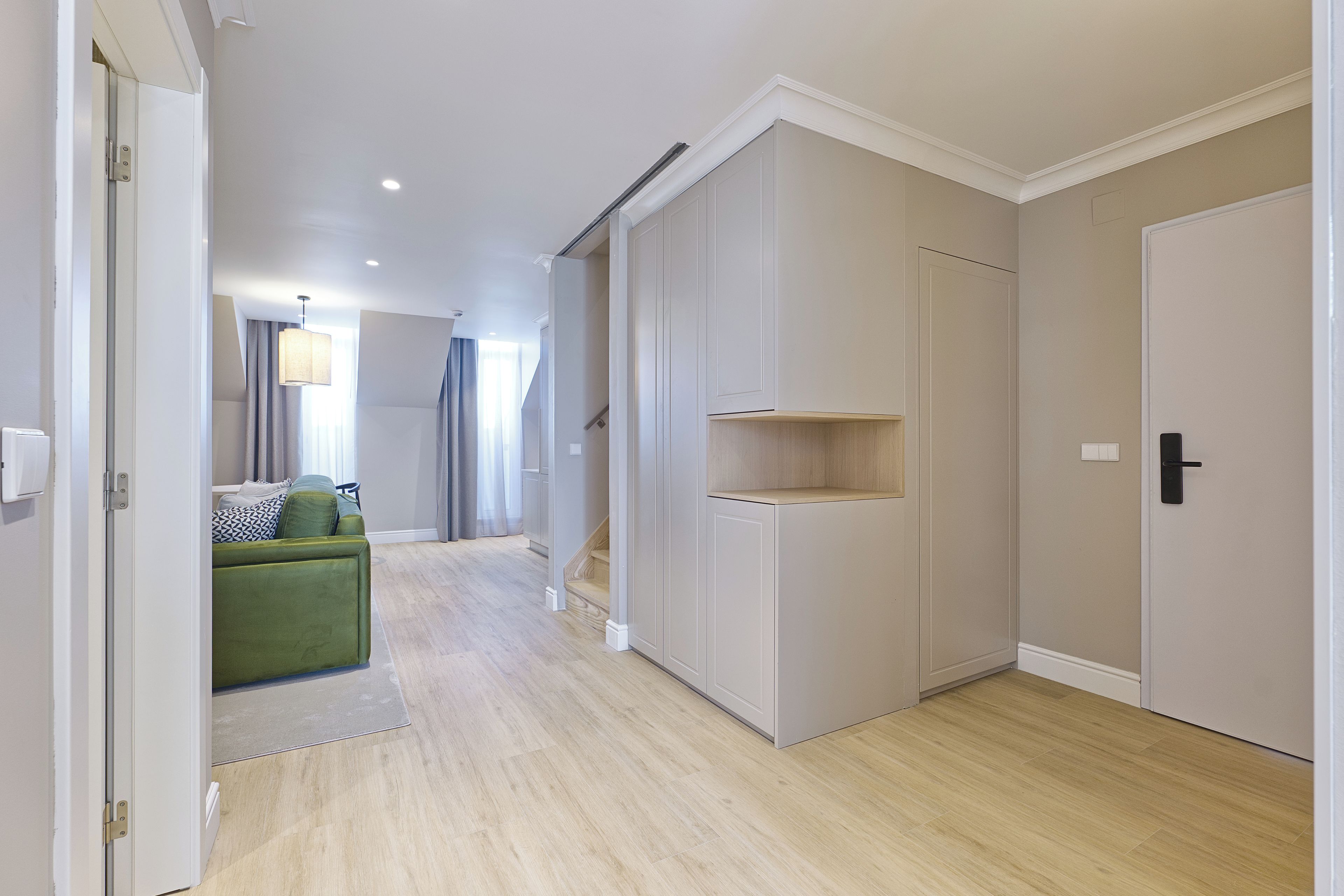 Un pasillo con un sofá verde, un armario blanco y una puerta que da a otra habitación.