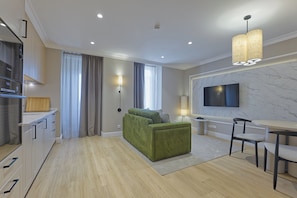 Una sala moderna con un sofá verde, un comedor con mesa y sillas, una cocina con electrodoméstico Bosch y un televisor grande montado en la pared.