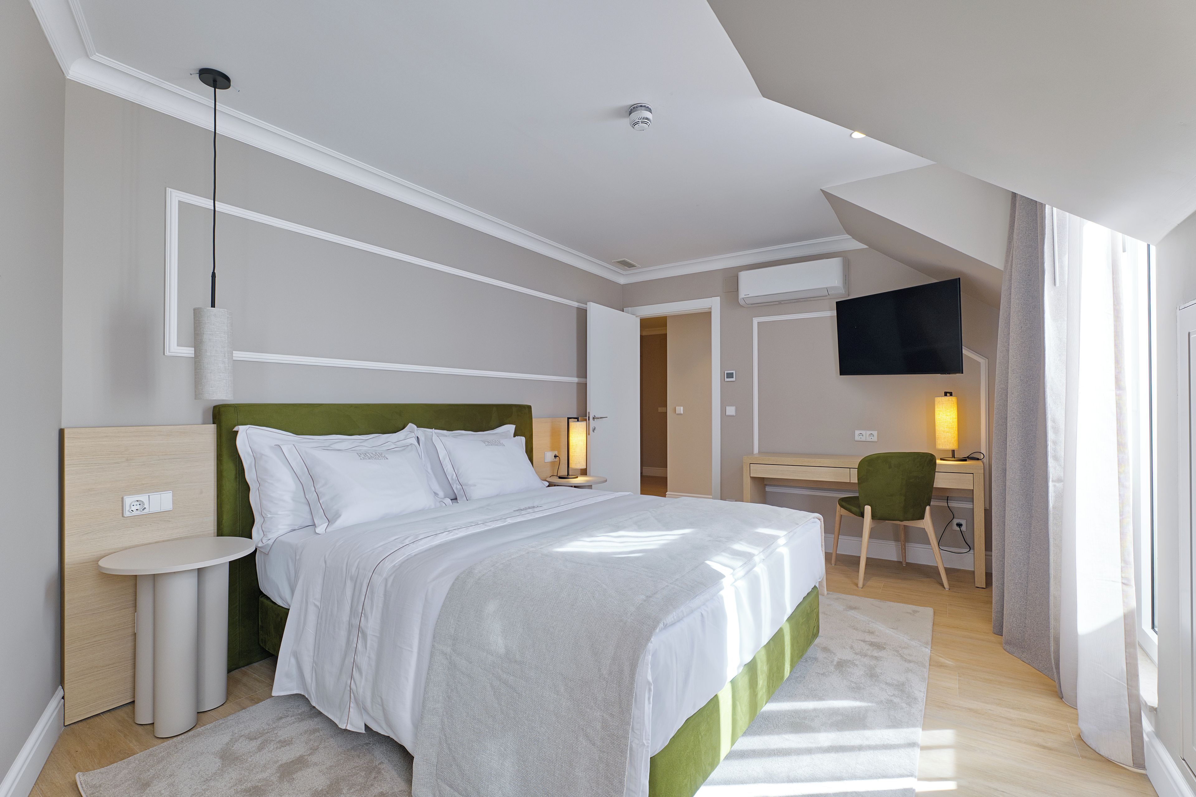 Quarto de hotel moderno com cama, mesas de cabeceira, escrivaninha, cadeira, televisão e janela.