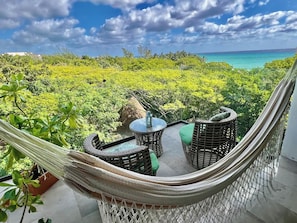A hammock chair with a table and cushions, overlooking a lush green landscape and a turquoise sea. - Ocean View at Mamitas Stunning (Playa del Carmen)