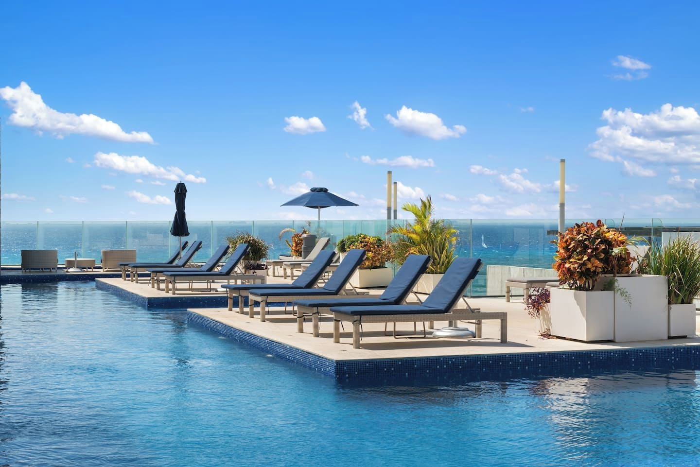 Une piscine à débordement située sur le toit, avec des chaises longues et des parasols, offrant une vue sur l’océan.