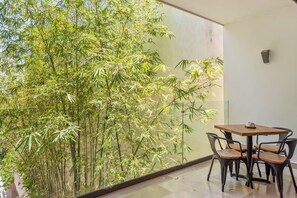 A balcony with a view of bamboo trees, a table with chairs, and a wall-mounted light fixture. - Mamitas Beach & 5 ta street | Pool & Ocean Views (Playa del Carmen)