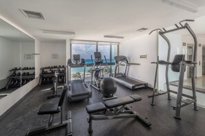 A gym with treadmills, weight machines, and dumbbells, overlooking a scenic view. - Mamitas Beach & 5 ta street | Pool & Ocean Views (Playa del Carmen)