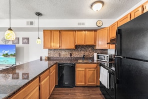 A modern kitchen with wooden cabinets, granite countertops, a black refrigerator, and a built-in oven. - Jamaica Daybreak North (Ocean City)