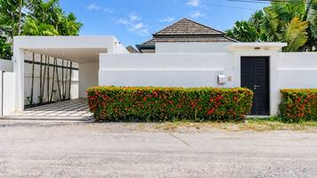 Una casa moderna con fachada blanca, puerta negra y un pequeño jardín con flores rojas.
