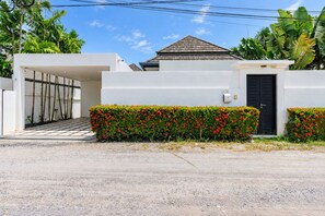 A modern house with a white exterior, a black door, and a small garden with red flowers. - 2 BR Pool Villa Clos Vougeot  (Muang Phuket)