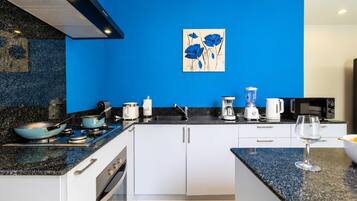 A modern kitchen with white cabinets, a blue backsplash, and a painting of blue flowers on the wall.