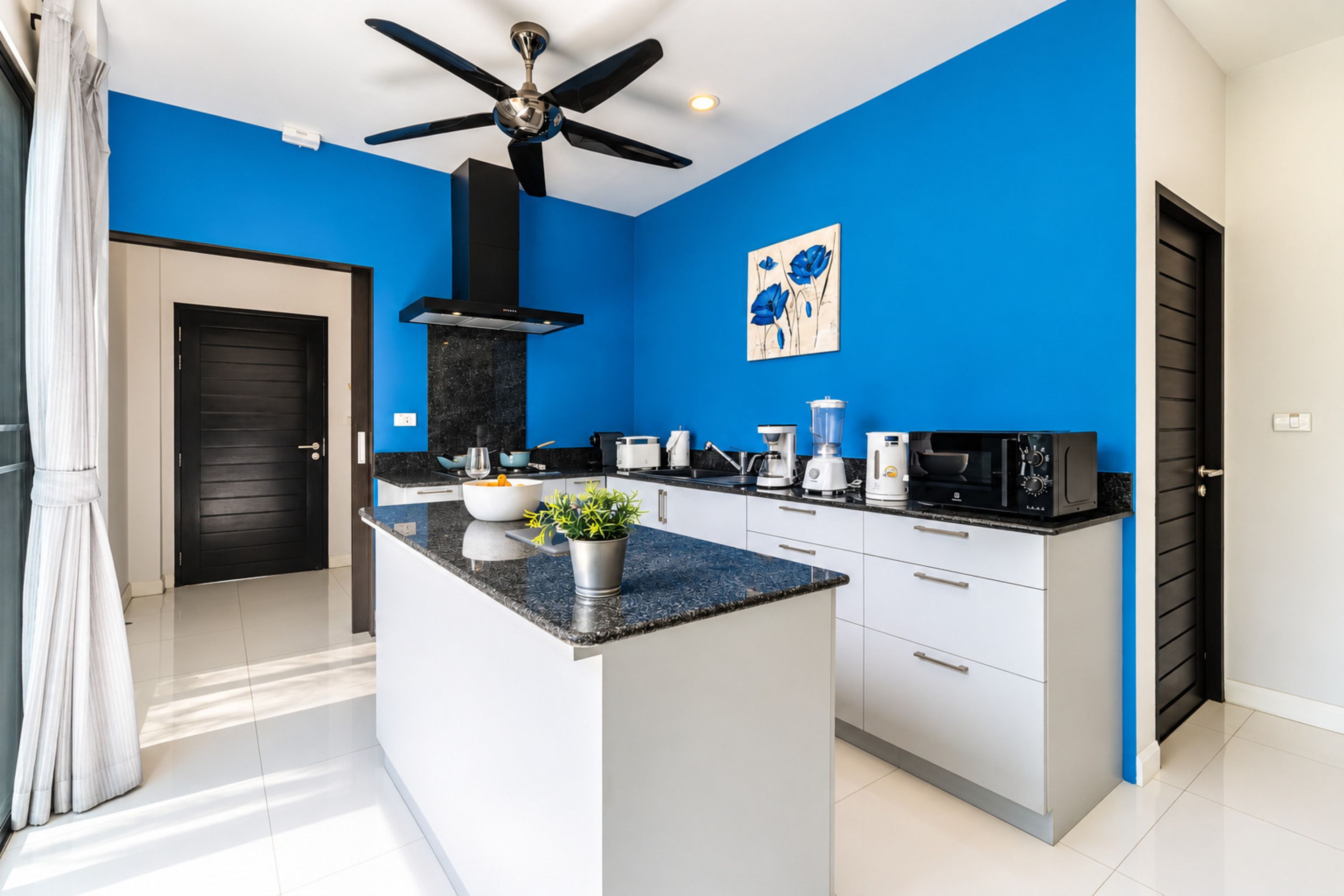 Une cuisine moderne dotée d’un îlot central, d’appareils électroménagers noirs et d’un ventilateur de plafond.
