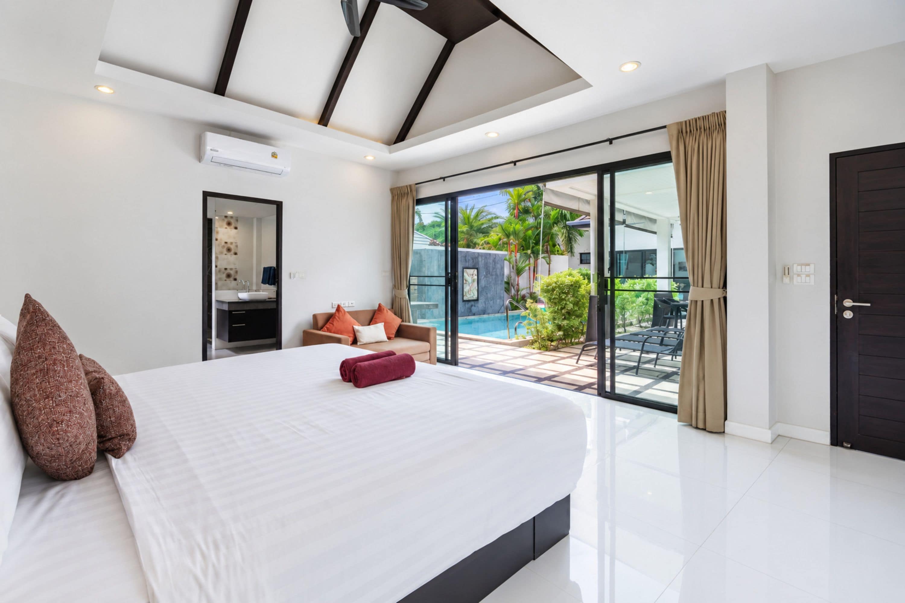 A modern bedroom with a large bed, a built-in air conditioning unit, a sliding glass door leading to a pool area, and a dark door.