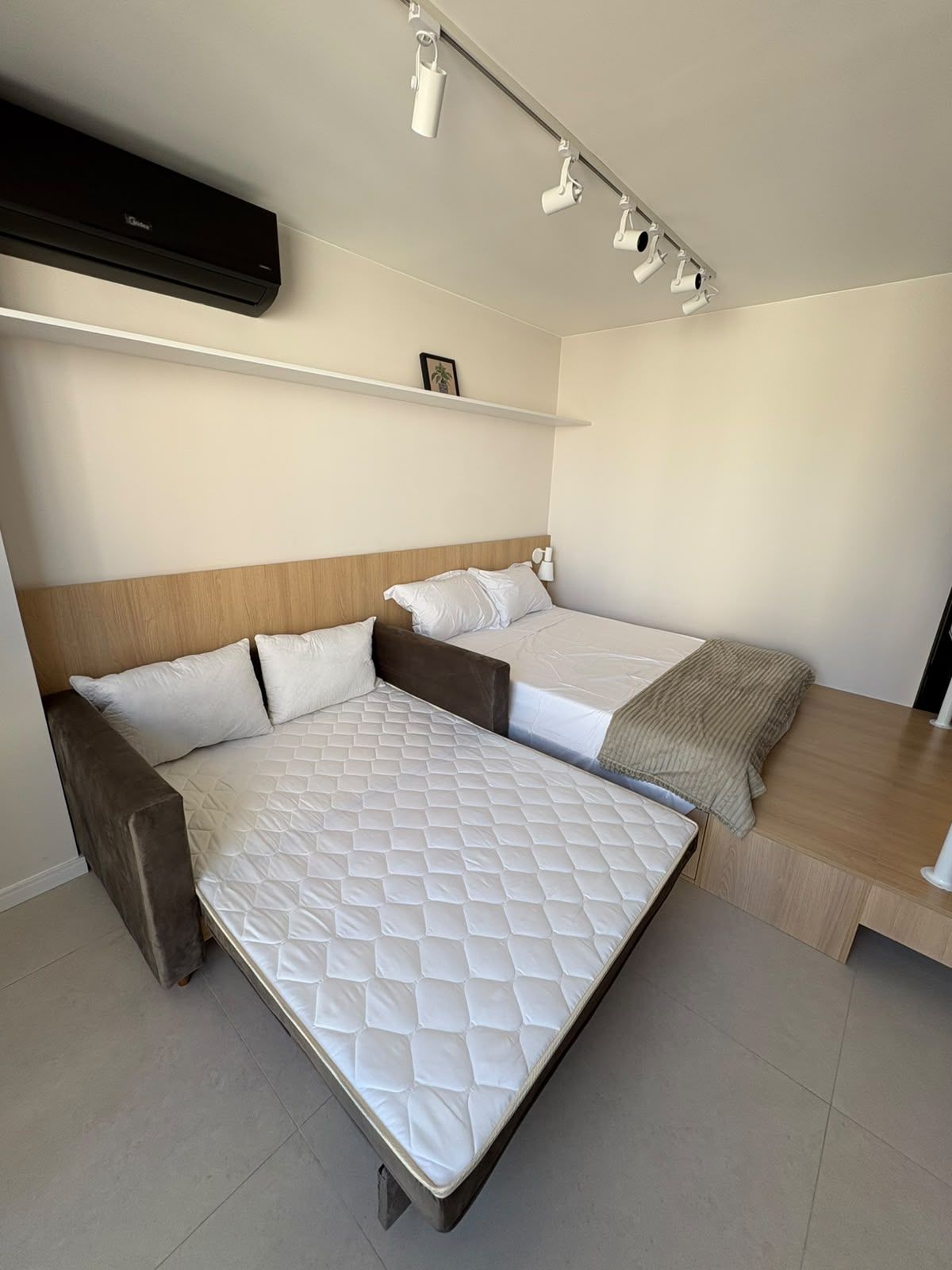 Ett modernt hotellrum med en dubbelsäng, en mindre säng, ett skrivbord och en väggmonterad luftkonditioneringsanläggning.