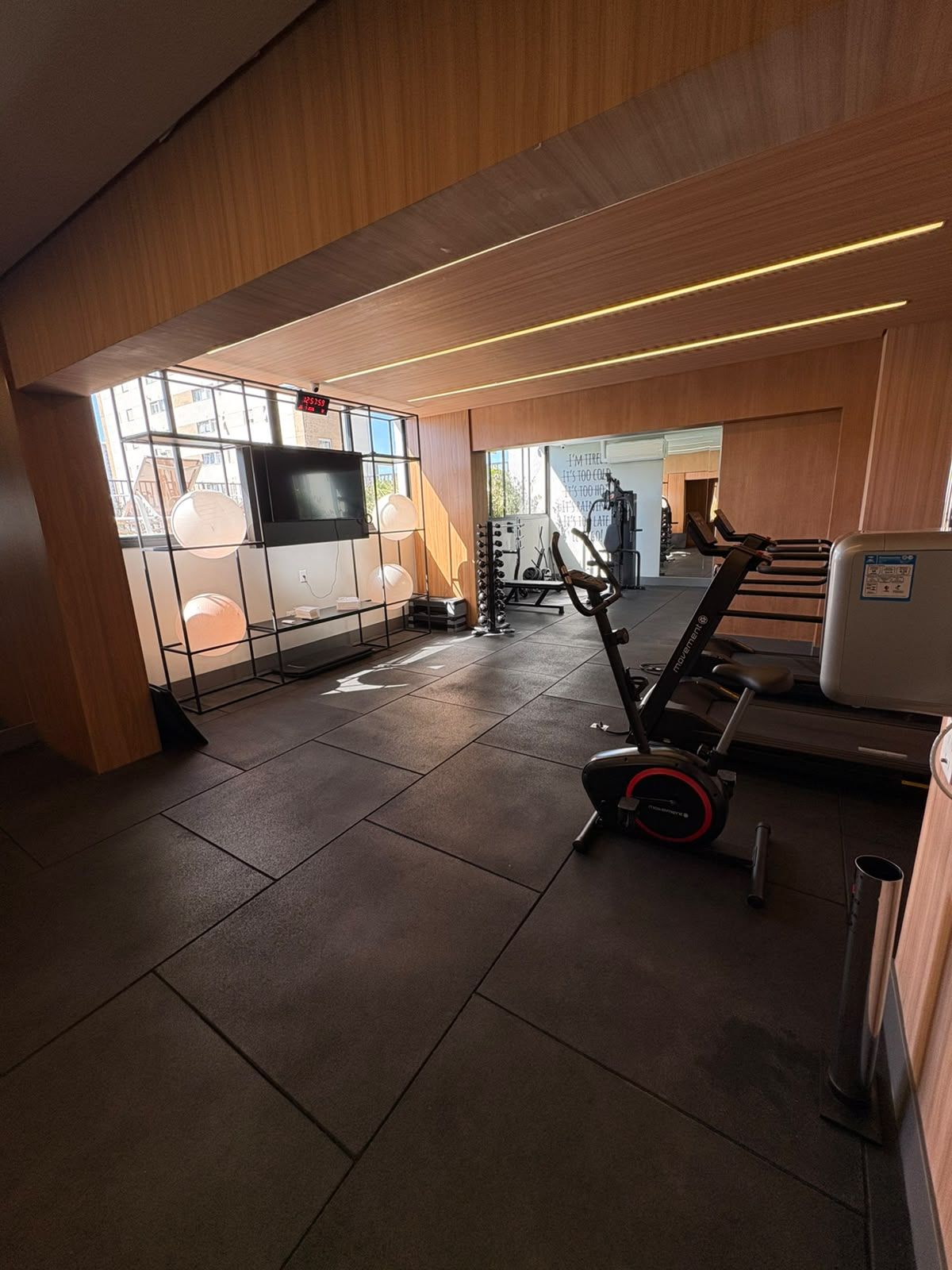 Ett gym med träningsutrustning, en tv och ett fönster med utsikt över byggnader.