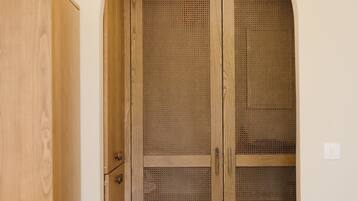 A wooden wardrobe with a mesh front, a wooden cabinet to the left, and a recessed ceiling light.