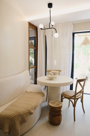 A modern interior with a round dining table, a wooden chair, a sofa, and a small wooden stool.