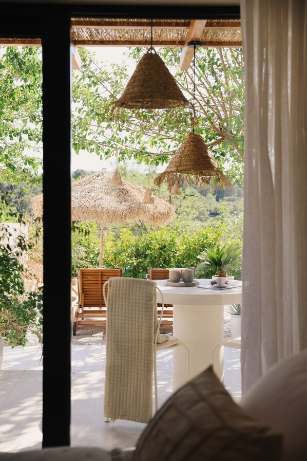 An outdoor seating area with a table, chairs, and thatched umbrellas, overlooking a lush landscape.